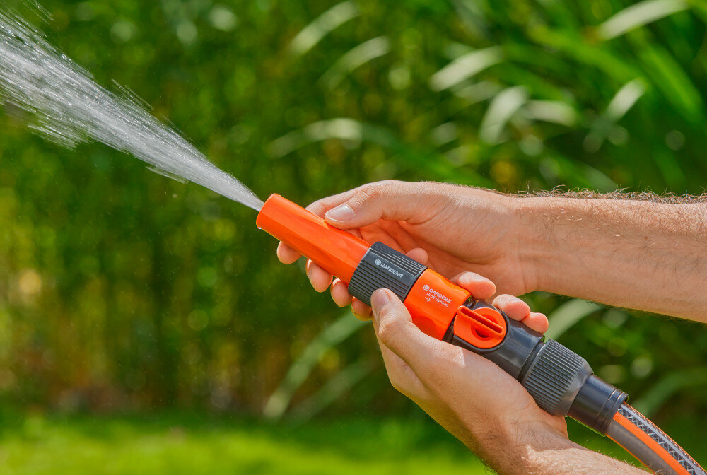 Pistolet zraszający GARDENA Profi-System 02818-20 osoba trzyma zraszacz w dłoni ze zraszacza płynie woda osoba reguluje przepływ wody w tle zielone rośliny strumień wody można płynnie dostosować do potrzeb delikatna mgiełka mocny strumień punktowy równomierne nawodnienie szybkie spłukiwanie zabrudzeń