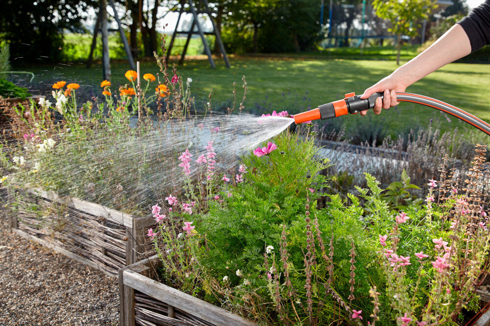 Pistolet zraszający GARDENA Profi-System 02818-20 ogród rabaty kwiatowe w tle drzewa domowy plac zabaw osoba podlewa kwiaty efektywne dozowanie wody możliwość regulacji strumienia precyzyjne podlewanie bez marnowania wody i energii