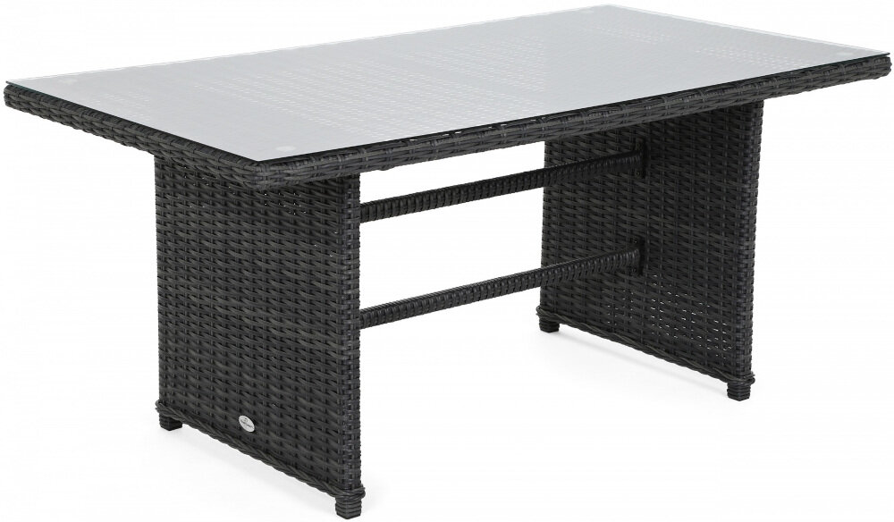 Stół ogrodowy z ciemnego rattanu z prostokątnym blatem z przezroczystego szkła. Konstrukcja stołu jest solidna, z dwoma pionowymi nogami połączonymi poziomymi belkami.