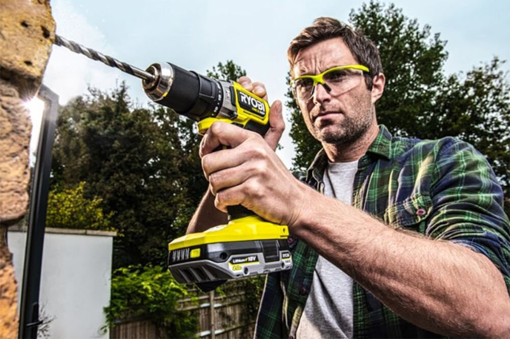 Akumulator RYOBI RB1820C 2Ah 18V, akumulator, zasilanie, 18V, Praca, Mężczyzna wierci w ścianie na dworze za pomocą wiertarki i wpiętym do niej akumulatorem