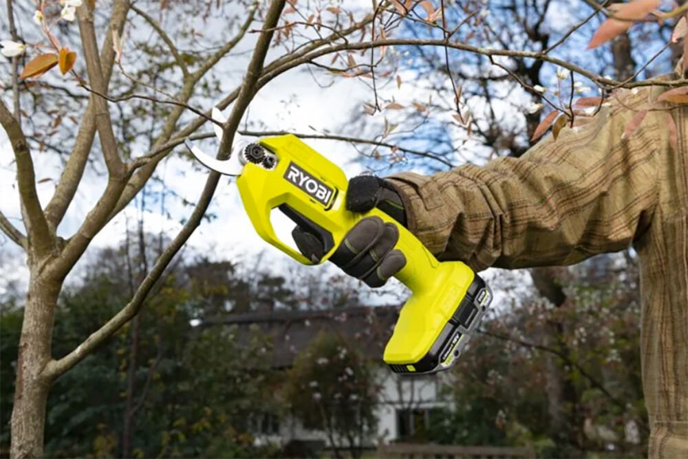 Akumulator RYOBI RB1820C 2Ah 18V, ONE+, model, akumulator, współpraca, Osoba przycina sekatorem gałęzie drzewa na działce, z wpiętym do sekatora akumulatorem