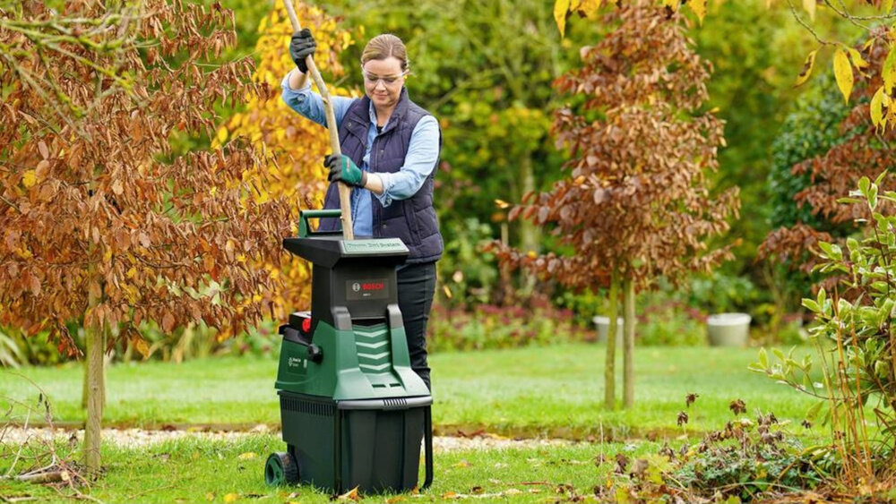 Rozdrabniacz do gałęzi BOSCH AXT 22 D 0600803003 ogród sad drzewa liście osoba upycha w rozdrabniaczu gałęzie porządek mobilność rozdrabnianie odpadków