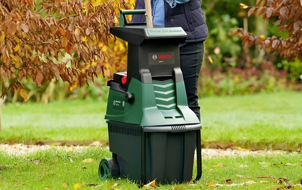 Rozdrabniacz do gałęzi BOSCH AXT 22 D 0600803003 ogród rozdrabniacz ustawiony na trawniku w tle drzewa system cięcia Drum Cut energiczne i bezproblemowe rozdrabnianie drewna o średnicy do 38 mm szybkie przetwarzanie oszczędność czasu mniejszy wysiłek