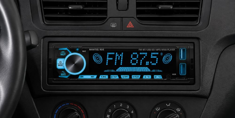 Obraz przedstawia radio samochodowe z wyświetlaczem pokazującym \'FM 87.5\'. Obok znajdują się ikony formatów plików: MP3, WMA, WAV, FLAC na tle fioletowych fal dźwiękowych.