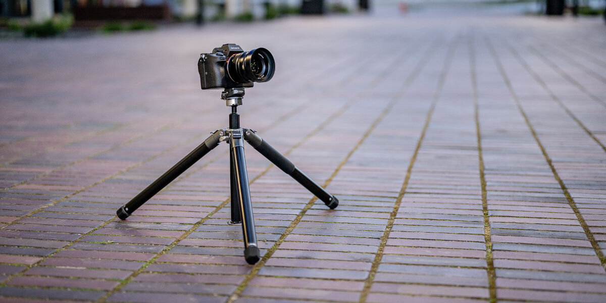 Statyw FOTOPRO Fly-1 Szary, centralna, kształt, złożenie, nogi, bliżej, na chodniku stoi statyw z niskim profilem z aparatem zamontowanym na nim