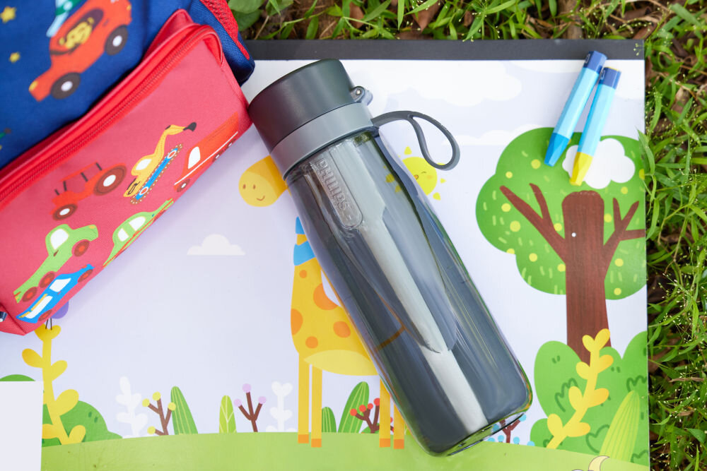 Butelka filtrująca PHILIPS GoZero AWP2731GRR/58 Ciemnoszara butelka filtrująca Philips leżąca na kolorowej macie dla dzieci obok czerwonego piórnika i kredek.