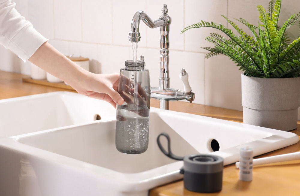 Butelka filtrująca PHILIPS GoZero AWP2731GRR/58 Napełnianie przezroczystej butelki Philips wodą z kranu w jasnej kuchni przy białym zlewozmywaku.