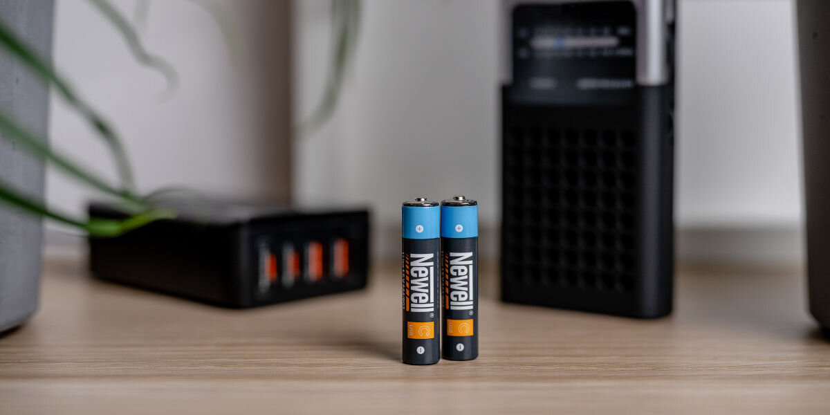 Akumulatorki AAA 500 mAh NEWELL (2 szt.), wygoda, minimalizm, ładowanie, podróż, akumulatorki stoją pionowo na stole, w tle powerbank