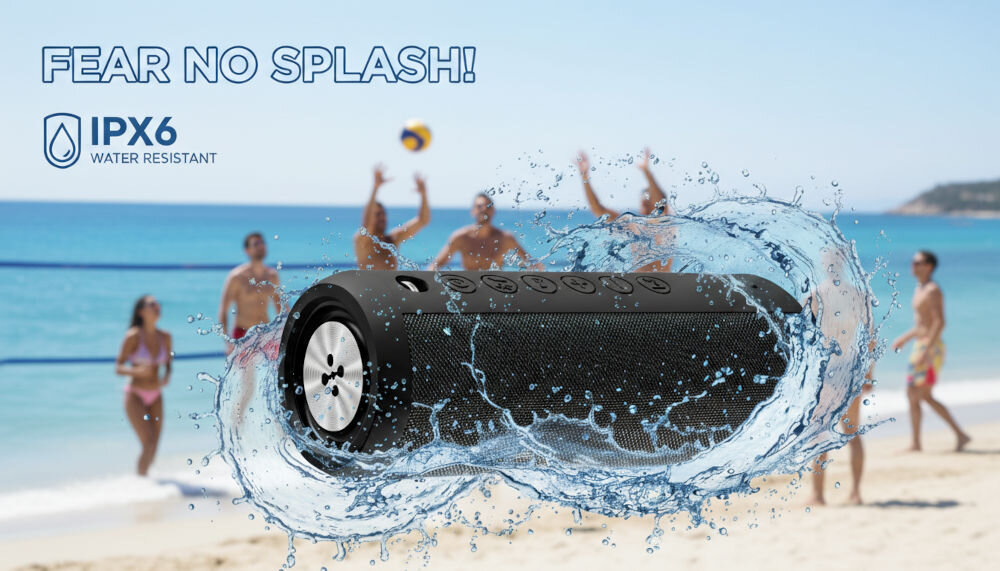 Głośnik mobilny XMUSIC BTS650K Wodoodporny głośnik Bluetooth z certyfikatem IPX6 otoczony bryzgami wody, w tle rozmazany widok plaży i osób grających w siatkówkę.