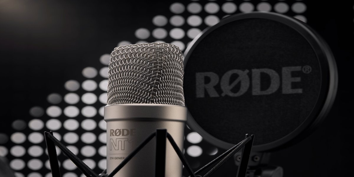 Na obrazie widoczny jest mikrofon z metalową siatką oraz pop filtr z logo RØDE. W tle znajdują się rozmyte białe kropki na czarnym tle.