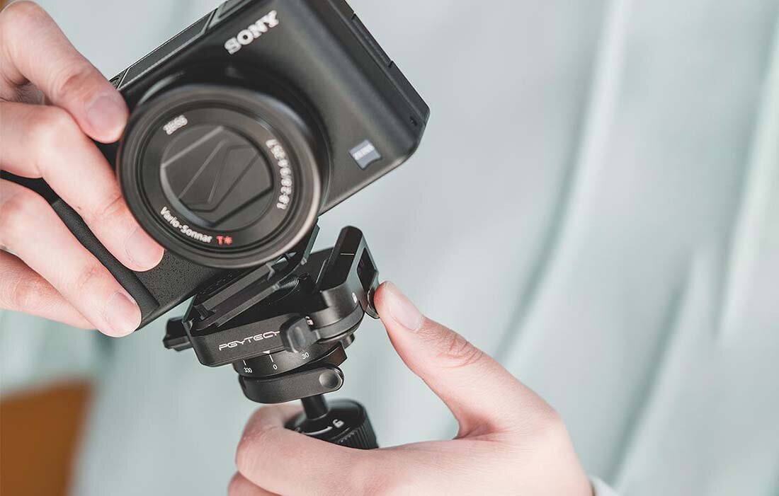 Osoba trzyma aparat fotograficzny zamocowany na szybkozłączce Pgytech Arca-Swiss. Na szybkozłączce widoczne jest logo \'PGYTECH\'.