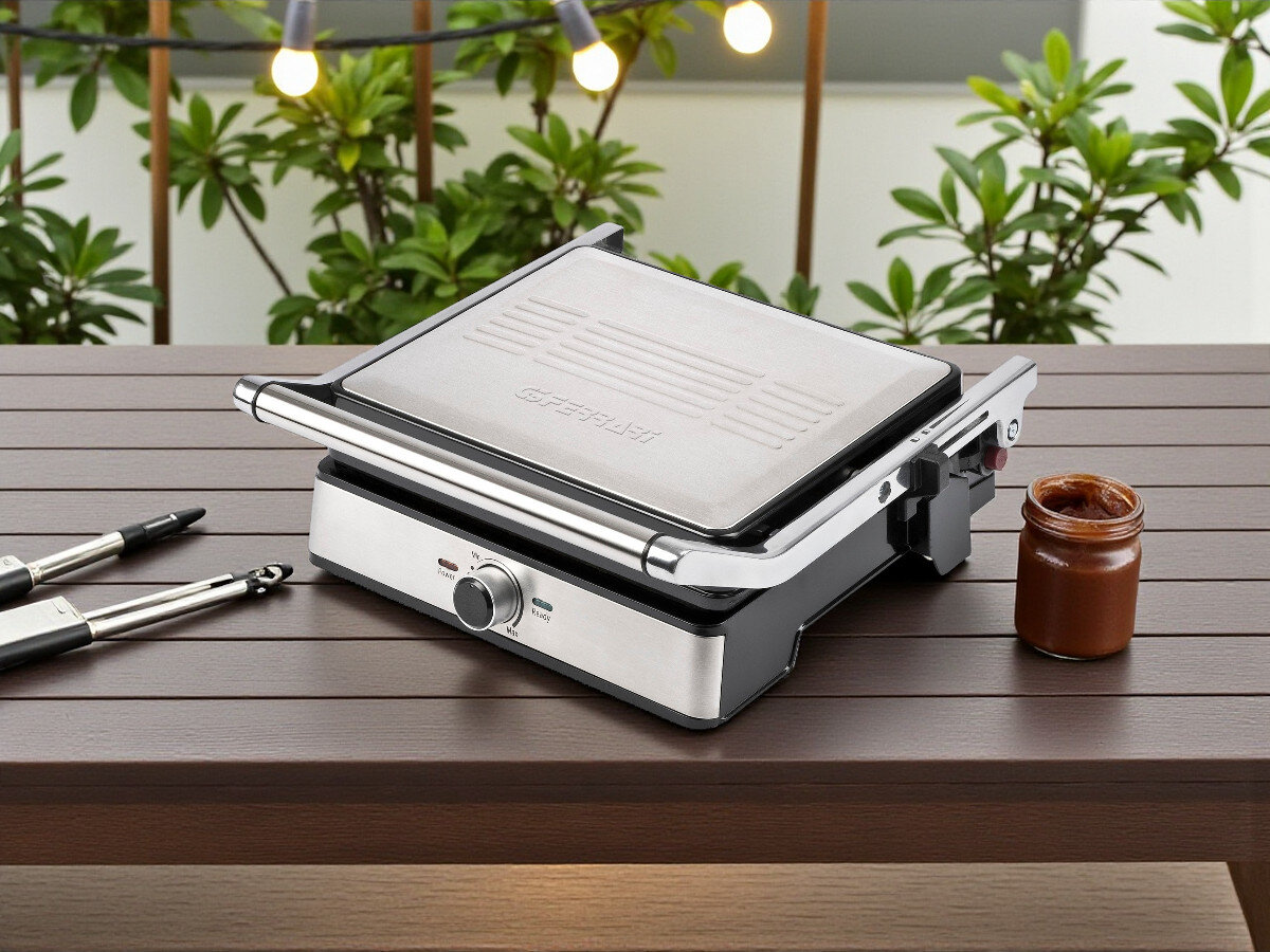 Grill elektryczny G3FERRARI Lavica Easy G10161, grillowanie, powierzchnia, wymiary, otwarcie, na drewninanym stole stoi grill z zamkniętą klapą górną frontem prawo skos