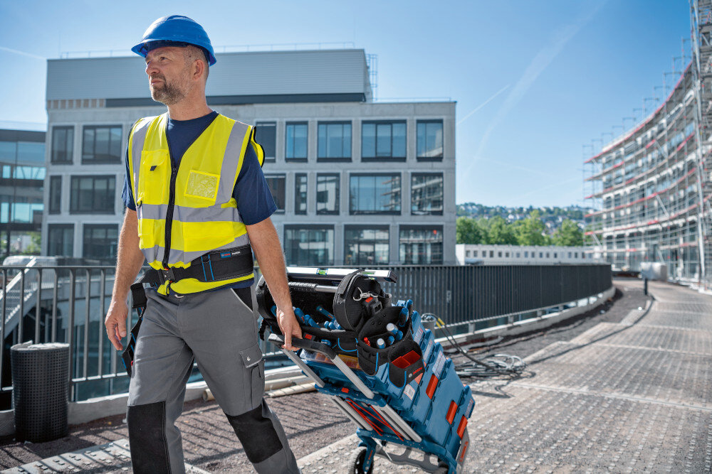 Torba narzędziowa BOSCH Professional GWT 20 miasto bloki osoba ciągnie za sobą wózek z walizkami na walizkach stoi torba w pełni kompatybilna z systemem Bosch Mobility spójne zestawy transportowe integracja z systemem ProClick mocowanie dodatkowych akcesoriów