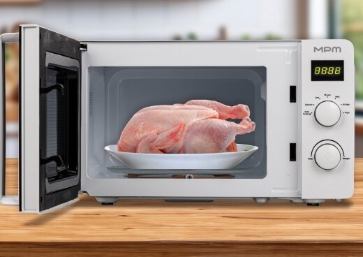Kuchenka mikrofalowa MPM-20-KMG-03/W z otwartymi drzwiczkami na kuchennym. W środku  surowy kurczak na talerzu.