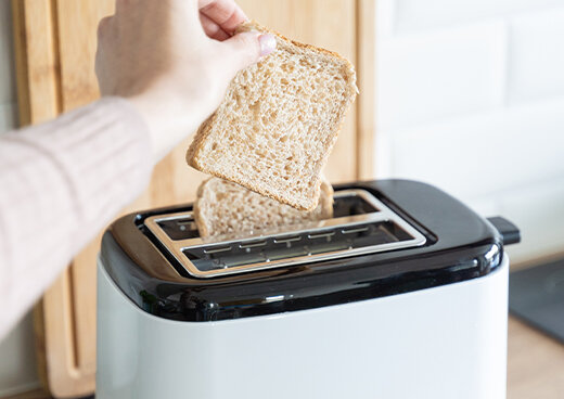 Osoba wkłada kromkę chleba do tostera MTO-07, w tle widać drugą włożoną już kromkę.