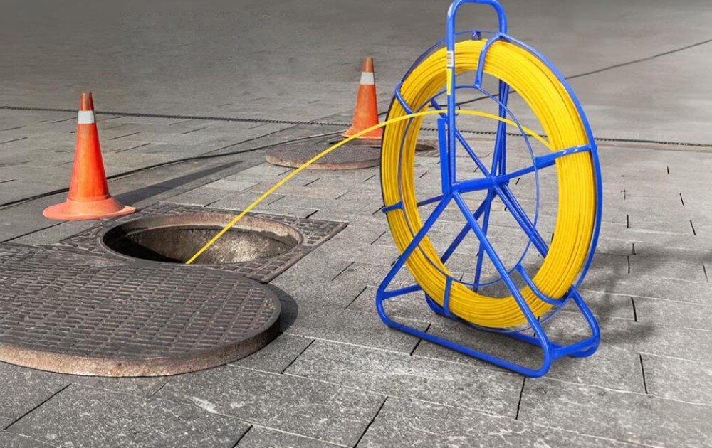 Pilot do przeciągania kabli EXTRALINK EX.31292 Niebieski stojak z żółtym przewodem ustawiony na ulicy z przewodem wchodzącym do studzienki kanalizacyjnej