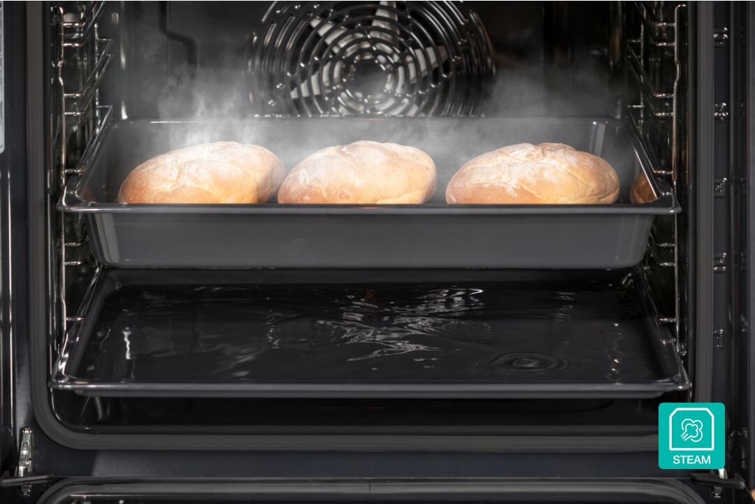 PIEKARNIK GORENJE BOS67371CLB Trzy bochenki chleba pieką się na blasze w piekarniku z aktywną funkcją pary, widoczną w postaci unoszącej się mgły. Ujęcie podkreśla równomierne wypiekanie i efekt chrupiącej skórki