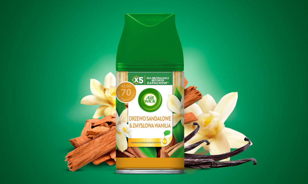 Zbliżenie na pojedynczy automatyczny odświeżacz powietrza Air Wick w opakowaniu z zieloną nakrętką i metalowym spodem. Etykieta przedstawia zapach DRZEWO SANDAŁOWE & ZMYSŁOWA WANILIA. Wokół produktu ułożone są naturalne składniki: laski cynamonu, kawałki drewna sandałowego oraz kwiaty i laski wanilii. Opakowanie podkreśla, że produkt zapewnia AŻ DO 70 DNI ŚWIEŻOŚCI i ma X5 SIŁĘ NEUTRALIZACJI UPORYCZONYCH ZAPACHÓW. Tło jest gradientowo zielone.