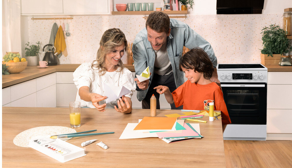 KUCHNIA GORENJE GECS6C70WC lifestyle kuchnia rodzina dziecko akcesoria plastyczne na stole kuchenka w tle kolor czarno srebrny okap półki czajnik akcesoria kuchenne na blacie