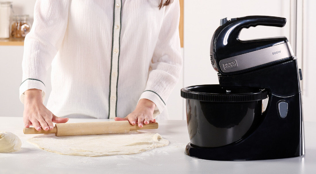 Osoba wałkuje ciasto na blacie, obok stoi czarny mikser z misą z logo \'BLACK&DECKER\' i oznaczeniem \'500W\'.