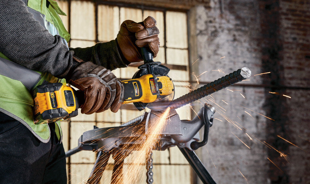 Szlifierka kątowa DEWALT DCG409H2T osoba używa szlifierki tnąc metalową rurkę do cięcia i szlifowania różnorodnych materiałów zasilanie akumulatorowe do pracy w warsztacie i na placu budowy pełna mobilność swoboda ruchu