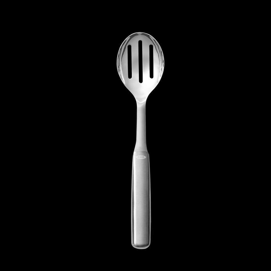 Na czarnym tle widoczna jest metalowa łyżka do serwowania z trzema otworami w części nabierającej. Na uchwycie znajduje się logo \'OXO\'.