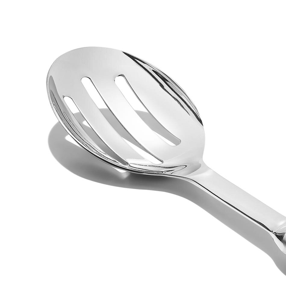 Na obrazie widoczna jest metalowa łyżka do serwowania z trzema podłużnymi otworami na powierzchni nabierającej. Łyżka ma błyszczącą, srebrną powierzchnię.