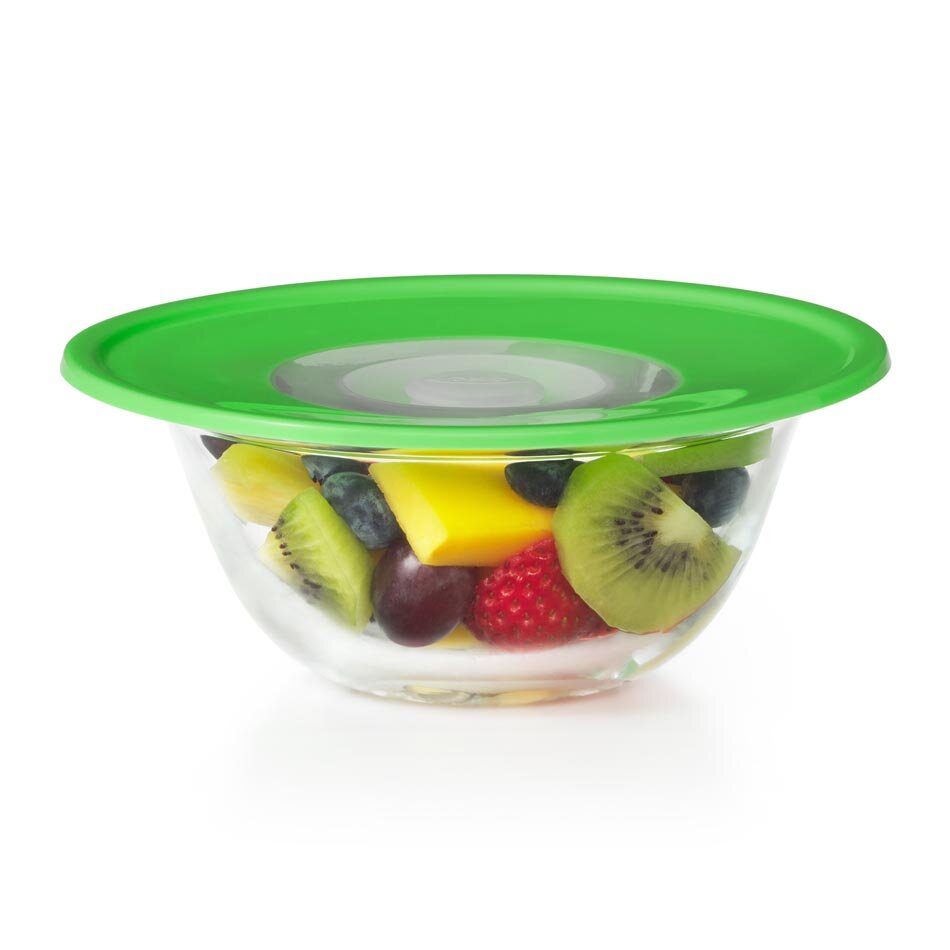 Przezroczysta miska wypełniona kawałkami owoców, przykryta zieloną silikonową pokrywką. W misce znajdują się kiwi, truskawki, winogrona i kawałki mango.