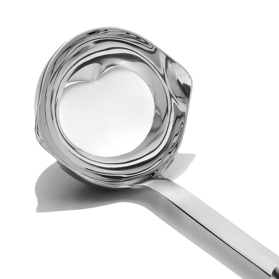 Na obrazie widoczna jest metalowa chochelka o błyszczącej powierzchni. Chochelka ma gładki, zakrzywiony uchwyt i okrągłą miseczkę.