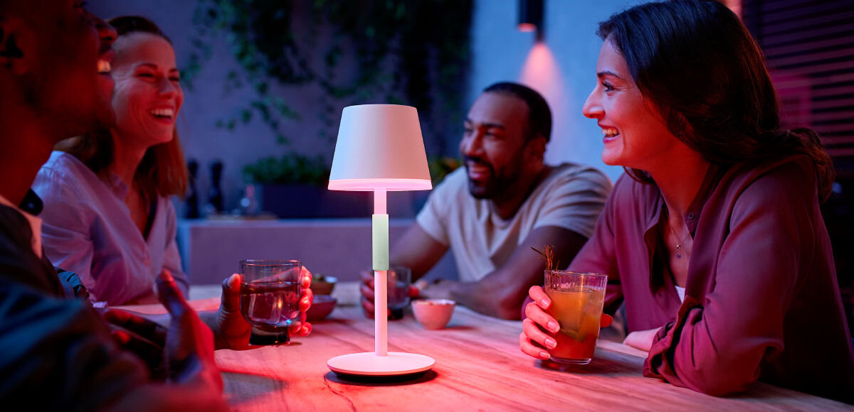Lampa stołowa PHILIPS HUE 929003128501 Czarny, kombinacje, oświetlenie, kolry, 16 milionów, 4 osoby siedzą przy stole z włączoną lampką wieczorową porą, rozmawiają