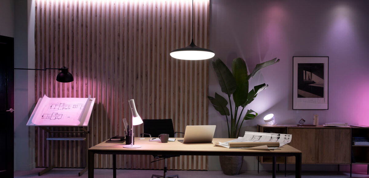 Lampa stołowa PHILIPS HUE 929003128501 Czarny, inteligentne, aplikacje, partnerzy, kompatybilność, Lampka stoi na stole w pomieszczeniu gościnnym, w tle różne barwy światła