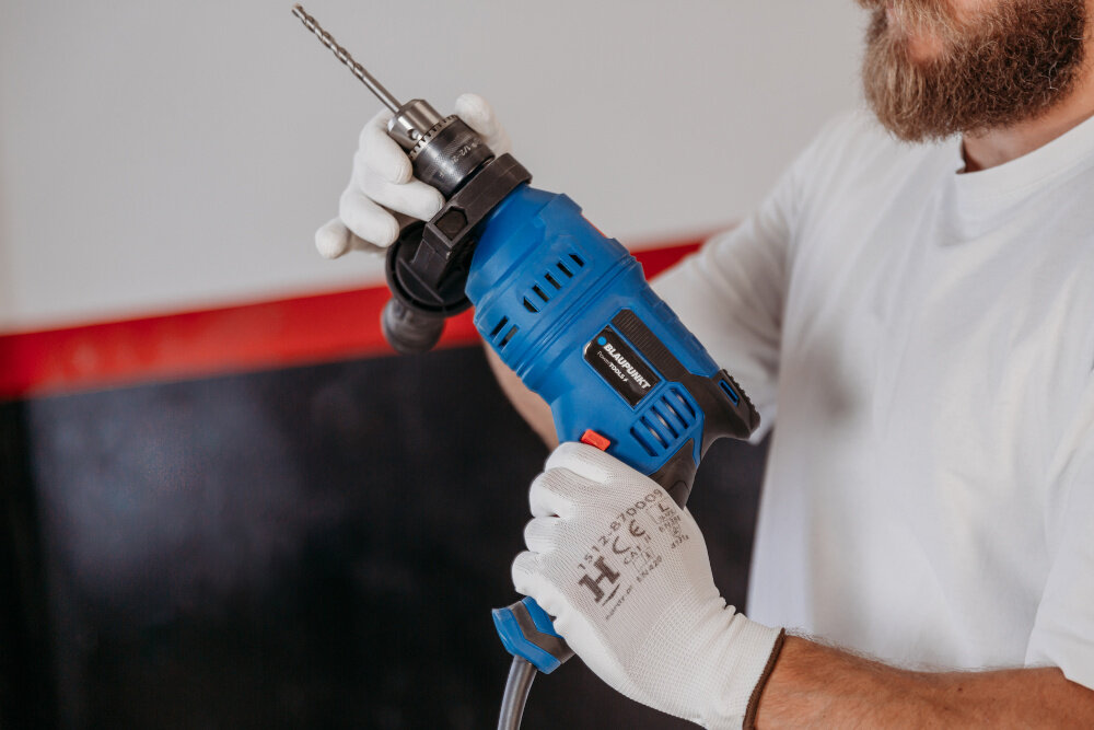 Wiertarka udarowa BLAUPUNKT ID8010 pomieszczenie osoba trzyma wiertarkę w dłoniach mocuje uchwyt w zestawie cztery wiertła do betonu o średnicach 4, 5, 6 i 8 mm praktyczny kluczyk do uchwytu wykonywanie różnorodnych prac