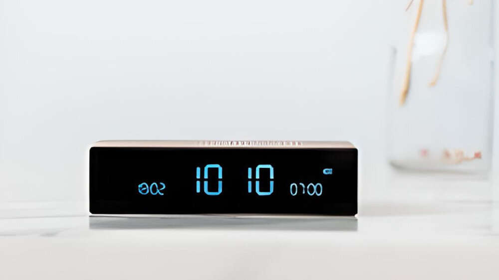 Złoty budzik z wyświetlaczem cyfrowym pokazuje godzinę 10:10 oraz czas alarmu 07:00. Obok widoczny jest symbol baterii i napis \'Snooze\'.