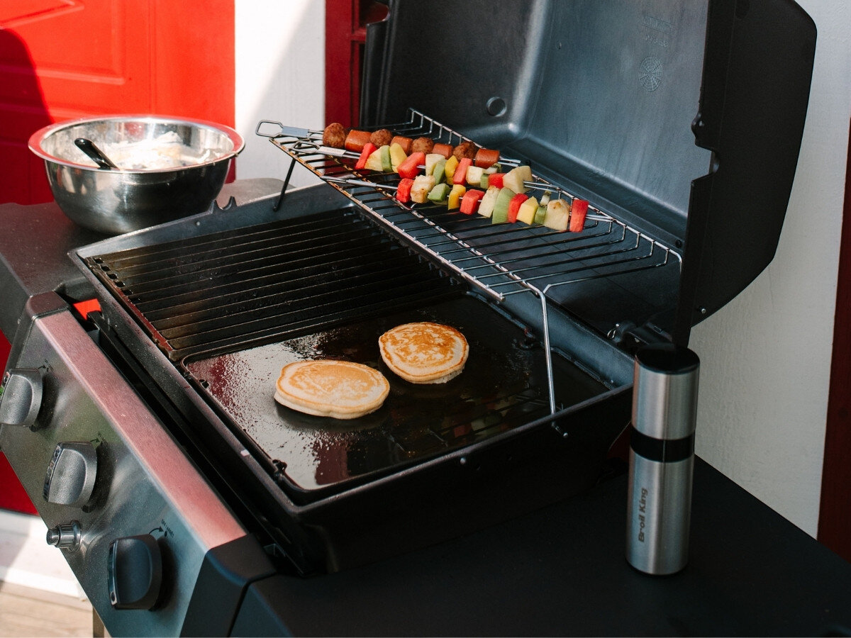 Płyta do grilla żeliwna BROIL KING GEM PORTA-CHEF 11237 33.5 x 26.5 cm, miejsce, powierzchnia, grillowanie, smażenie, Dwa naleśniki smażą się na gładkiej żeliwnej płycie położonej na ruszcie grilla, obok na górnym poziomie leżą szaszłyki warzywne i mięsne.