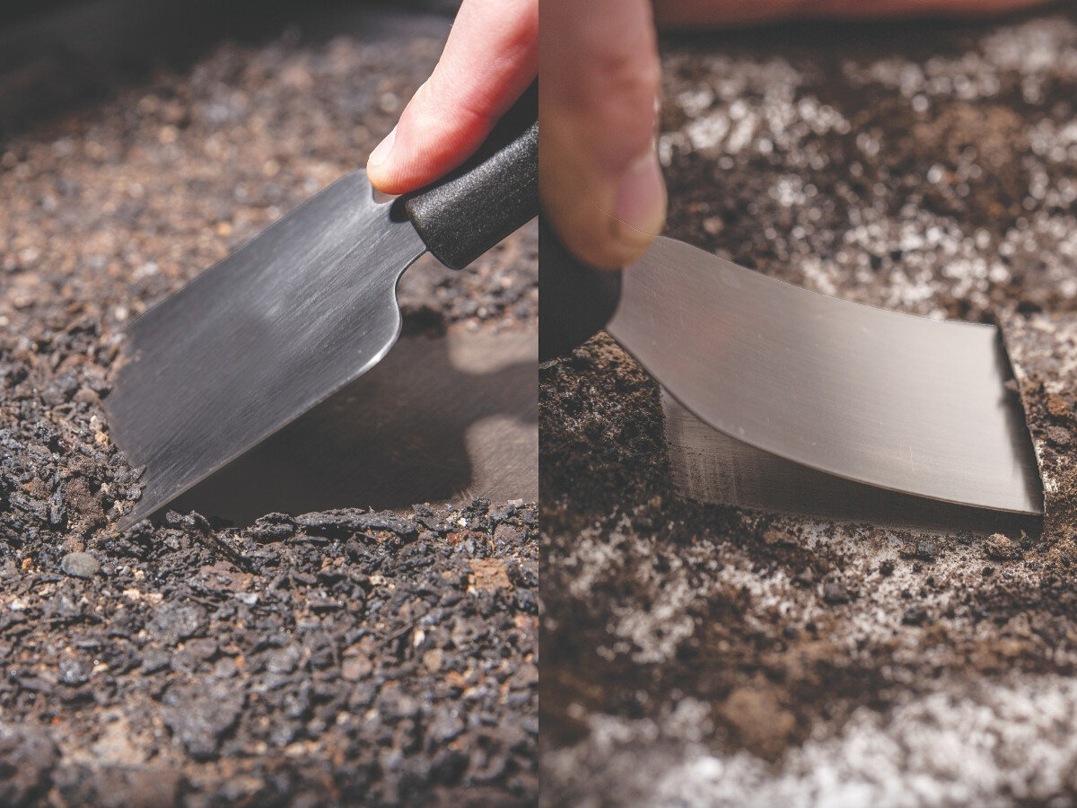 Na obrazie widoczne są dwie metalowe szpatułki z czarnymi uchwytami, używane do czyszczenia powierzchni pokrytej resztkami jedzenia i przypaleniami.