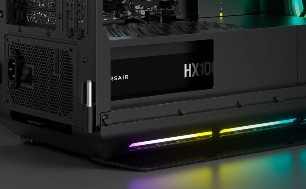 Zasilacz CORSAIR HX1000i Wnętrze obudowy komputera z widocznym zasilaczem umieszczonym w dolnej części i podświetleniem RGB biegnącym wzdłuż dolnej krawędzi podstawy, opis