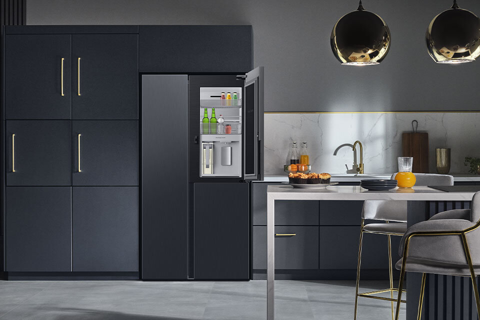 Zdjęcie pokazujące lodówkę Samsung z centrum napojów stojącą w przestronnej i nowocześnie urządzonej kuchni