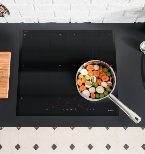 Płyta indukcyjna Amica na blacie kuchennym, na niej patelnia wypełniona warzywami
