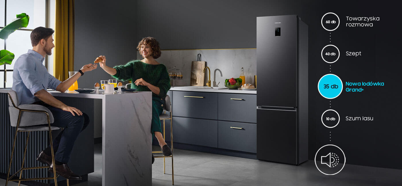W kuchni przy stole siedzą dwie osoby, a obok stoi grafitowa lodówka. Na obrazie widoczny jest tekst: \'60 db Towarzyska rozmowa\', \'40 db Szept\', \'35 db Nowa lodówka Grand+\', \'10 db Szum lasu\'.