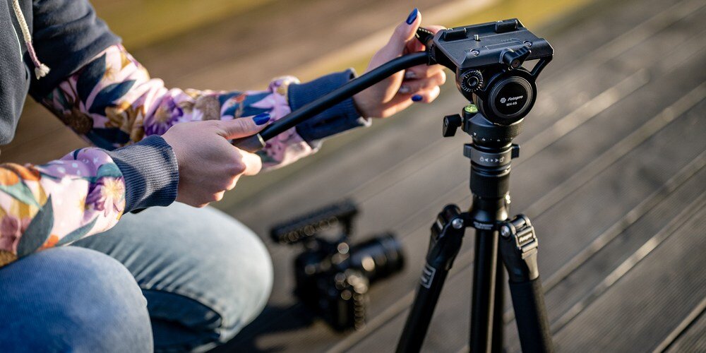 Kobieta siedzącą na schodach ustawia głowicę pod odpowiednim kątem. W tle aparat, który będzie montowała na statywie.