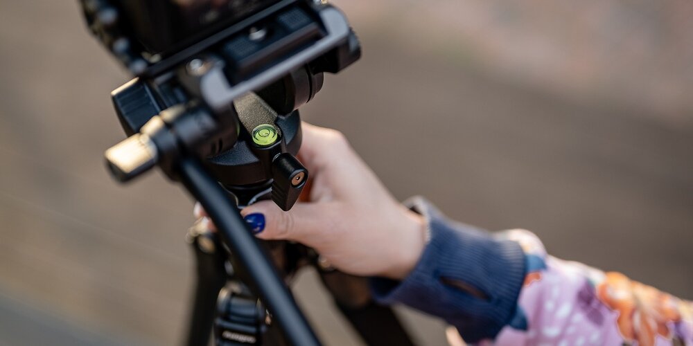 Zbliżenie na głowicę poziomującą statywu Fotopro S5i Pro i damską rękę trzymającą za tenże statyw.