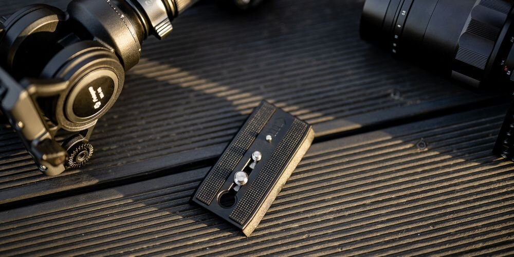 Płytka montażowa do statywu Fotopro S5i Pro na ciemnych deskach kompozytowych. W tle fragment aparatu i głowica do statywu.