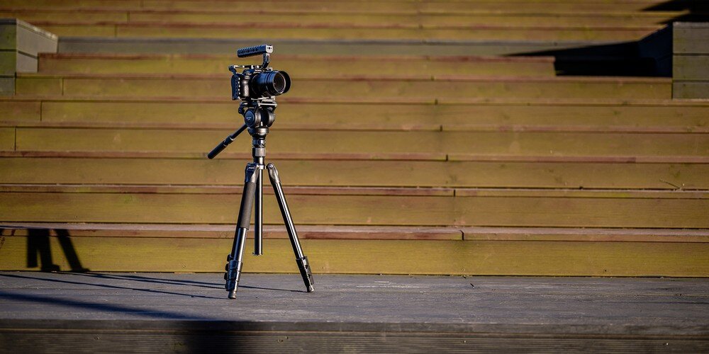 Aparat na niskim statywie fotograficznym ustawiony na drewnianych schodach.