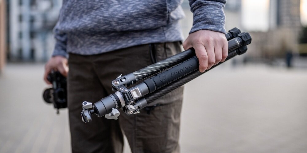 Statyw Fotopro X-Aircross 3, złożony, trzymany w dłoni na zewnątrz; kompaktowy, karbonowy, do fotografii mobilnej, w mieście.