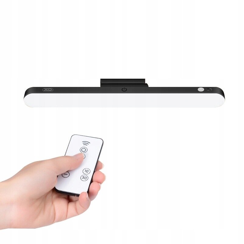 Czarna lampa magnetyczna LED z białym panelem świetlnym, posiada logo \'XO\' oraz przycisk zasilania. Obok widoczny jest pilot z trzema przyciskami, trzymany w dłoni.