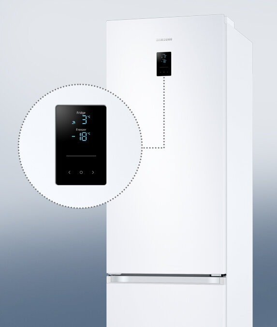 Biała lodówka z wyświetlaczem na drzwiach, pokazującym temperatury: Fridge 3°C, Freezer -18°C. Logo \'SAMSUNG\' widoczne na górze lodówki.