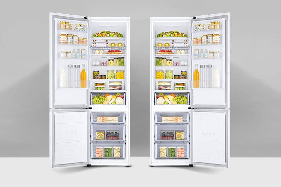 Dwie białe lodówki z otwartymi drzwiami, wypełnione różnorodnymi produktami spożywczymi, takimi jak owoce, warzywa, napoje i słoiki. W dolnej części znajdują się zamrażarki z przeźroczystymi szufladami pełnymi mrożonek.