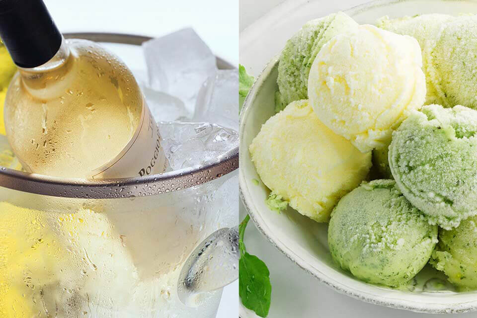 Po lewej stronie znajduje się butelka wina zanurzona w wiaderku z lodem, a po prawej miska z kulkami lodów w kolorach żółtym i zielonym.