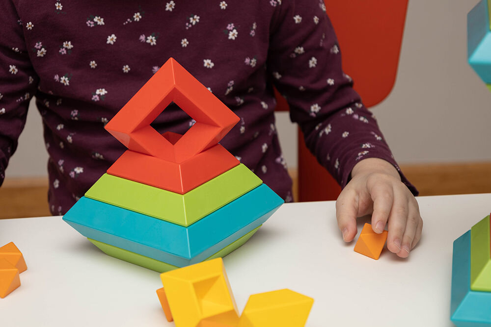 Dziecko budujące geometryczną piramidę z kolorowych klocków Rubanta; na pierwszym planie czerwony element w kształcie rombu.
