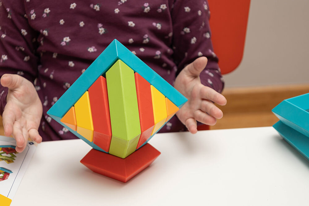 Prezentacja ukończonej, wielokolorowej kompozycji z klocków pitagorejskich ustawionej pionowo na czerwonej podstawie.